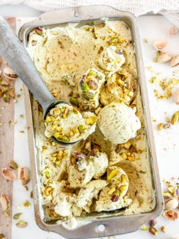 No Churn Pistachio Ice Cream in metal bread pan with ice cream scoop on white marble close up
