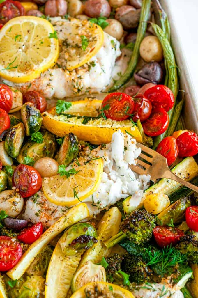 Sheet Pan Cod Vegetable Dinner with gold fork and lemon slices on white marble