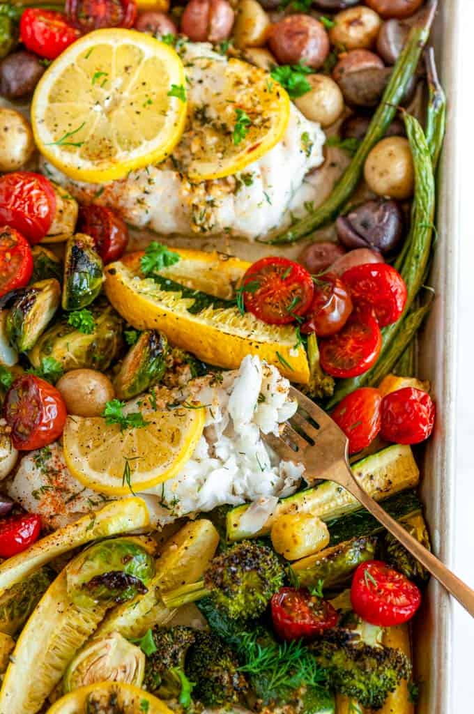 Sheet Pan Cod Vegetable Dinner with gold fork and lemon slices on white marble