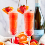 Sunrise Strawberry Mimosa Cocktail in glasses with oranges and Prosecco bottle in background on white marble