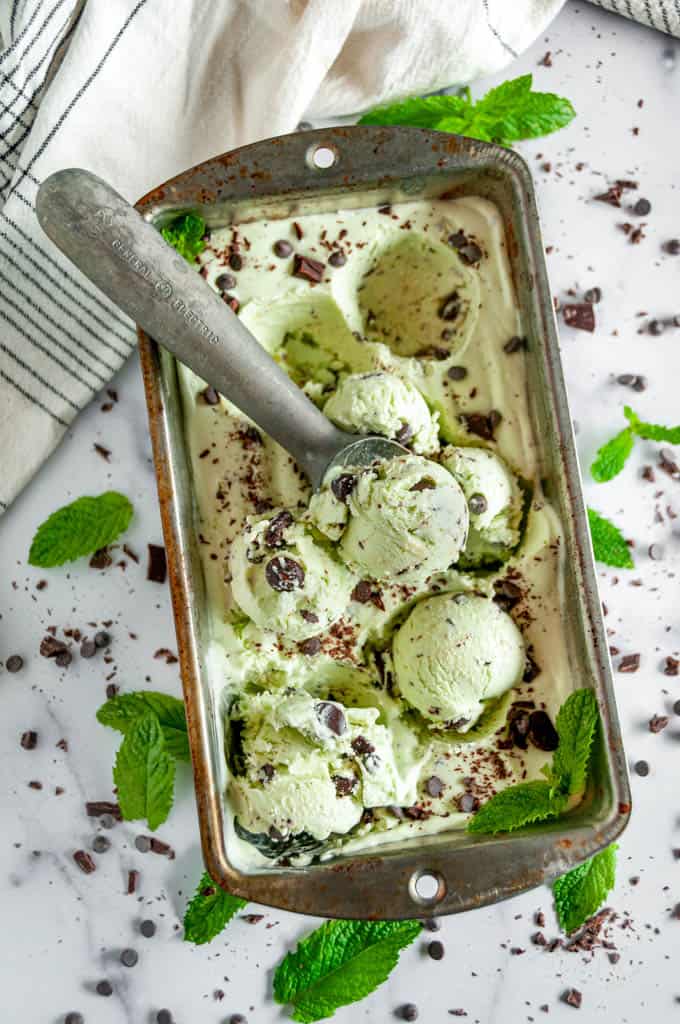 No Churn Mint Chocolate Chip Ice Cream with scoop and tea towel in silver bread pan on white marble