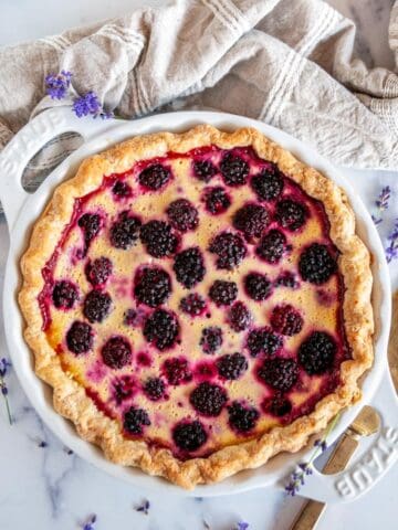 Blackberry Lavender Custard Tart with gold pie server and tea towel on white marble
