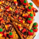 Halloween Pumpkin Cheesecake topped with chocolate drizzle and candy corn on white cake plate