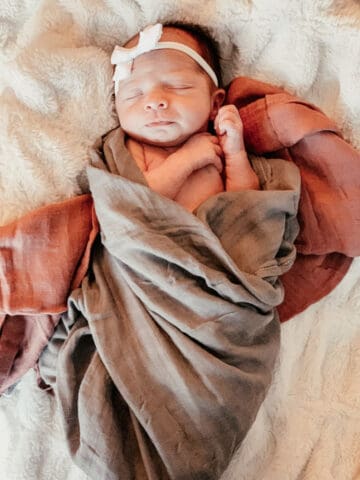 Newborn baby swaddled in red and gray blankets