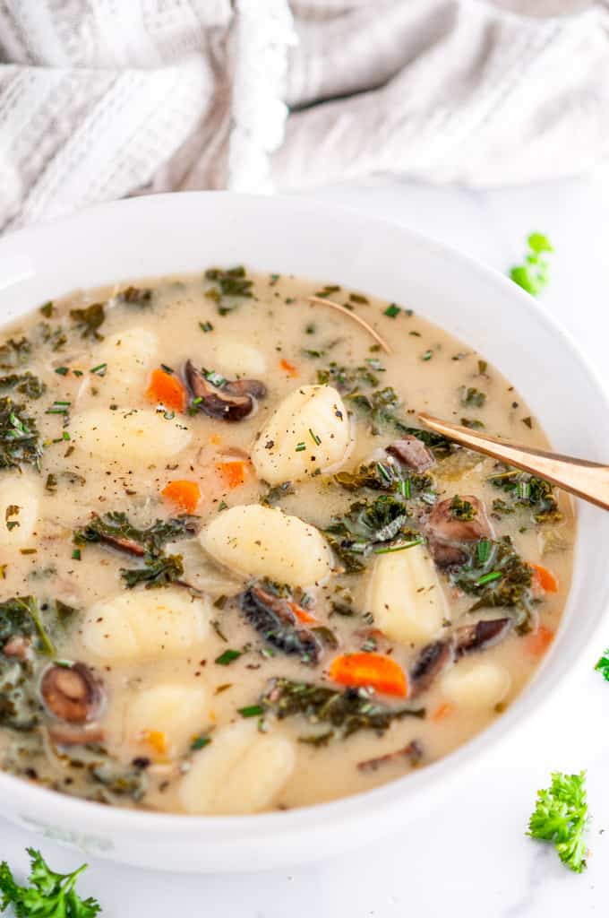 Vegetarian Gnocchi Kale Soup in white bowl with gold spoon and tea towel on white marble