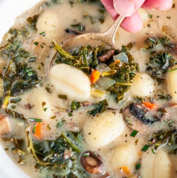Vegetarian Gnocchi Kale Soup in white bowl with gold soon held in hand close up