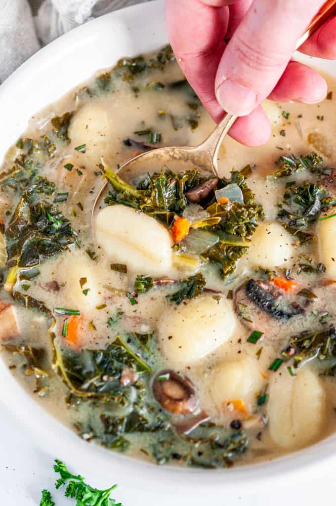 Vegetarian Gnocchi Kale Soup in white bowl with gold soon held in hand close up
