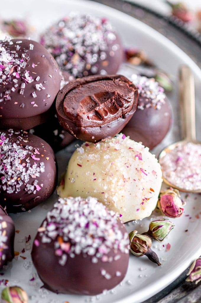 Decadent Dark Chocolate Rose Truffles with bite sprinkled with rose buds and sanding sugars on white plate