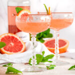 Pink Pamplemousse Gin Cocktail in crystal glasses with fresh mint and Giffard liqueur bottle on white marble