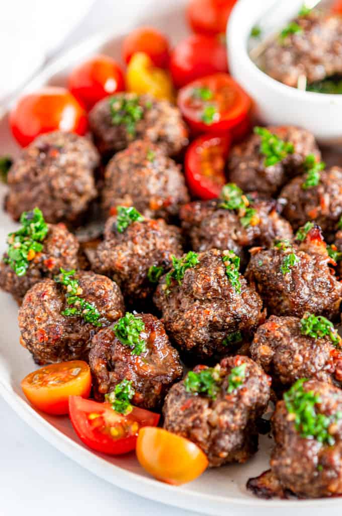 Sheet Pan Italian Meatballs with Chimichurri Sauce on white plate with halved cherry tomatoes