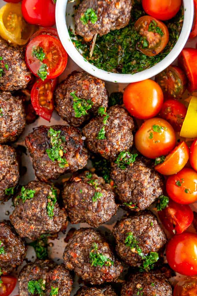 Sheet Pan Italian Meatballs with Chimichurri Sauce on white plate with halved cherry tomatoes