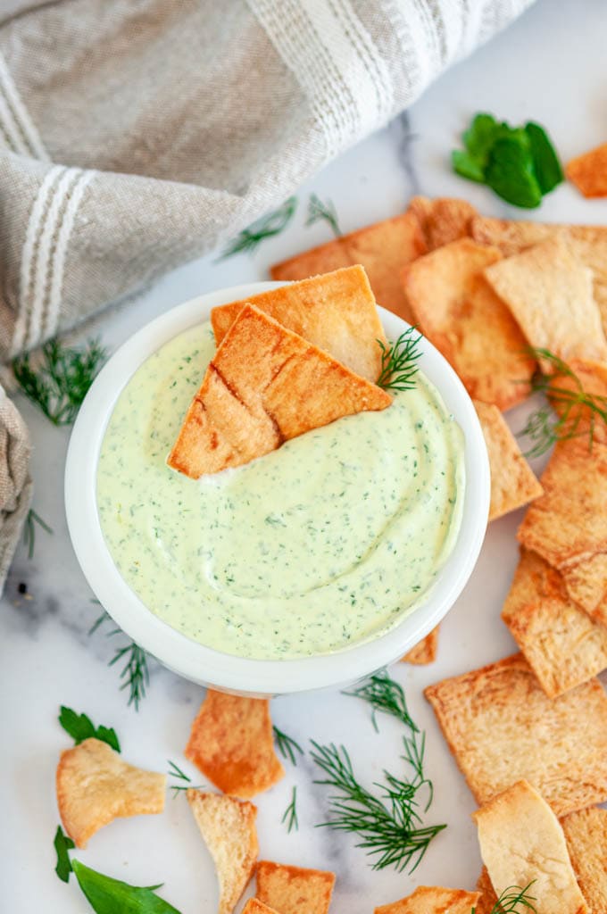 Creamy Garlic Herb Cheese Dip in white bowl with pita chips and tea towel on marble