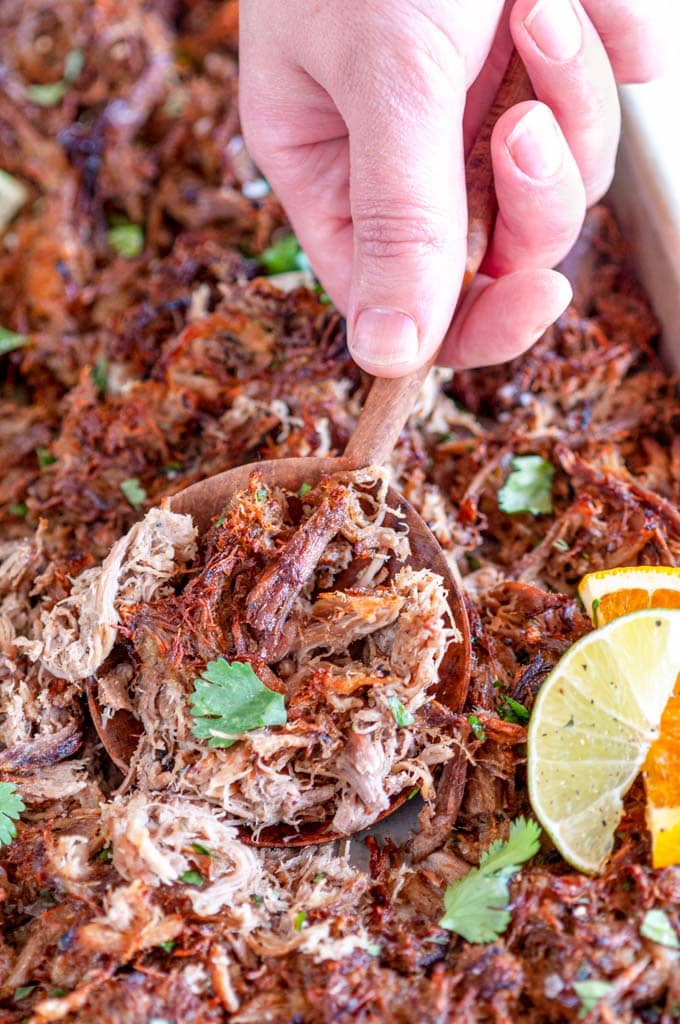 Cuban Inspired Instant Pot Pulled Pork on sheet pan with wooden spoon held in hand and citrus slices