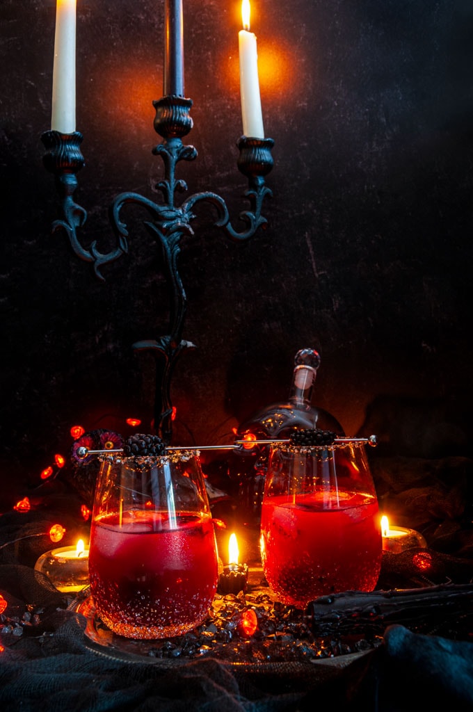 Halloween Black Cranberry Margarita in stemless glass with sanded sugar rims on black cloth and candle background