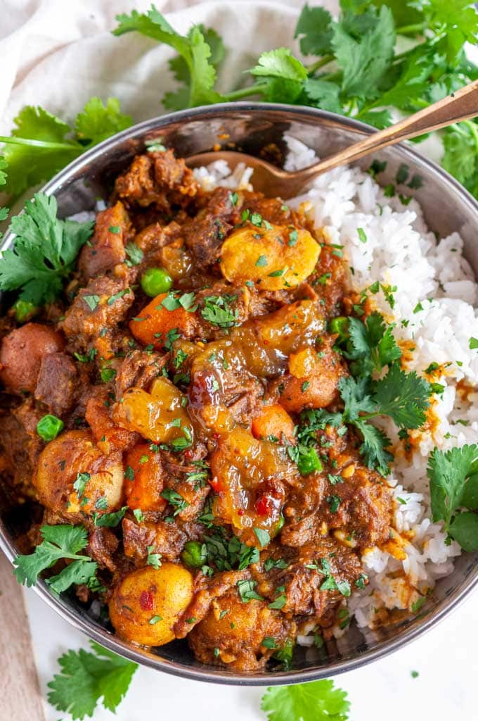 Instant Pot Beef Curry in silver bowl with basmati rice and fresh cilantro on white marble