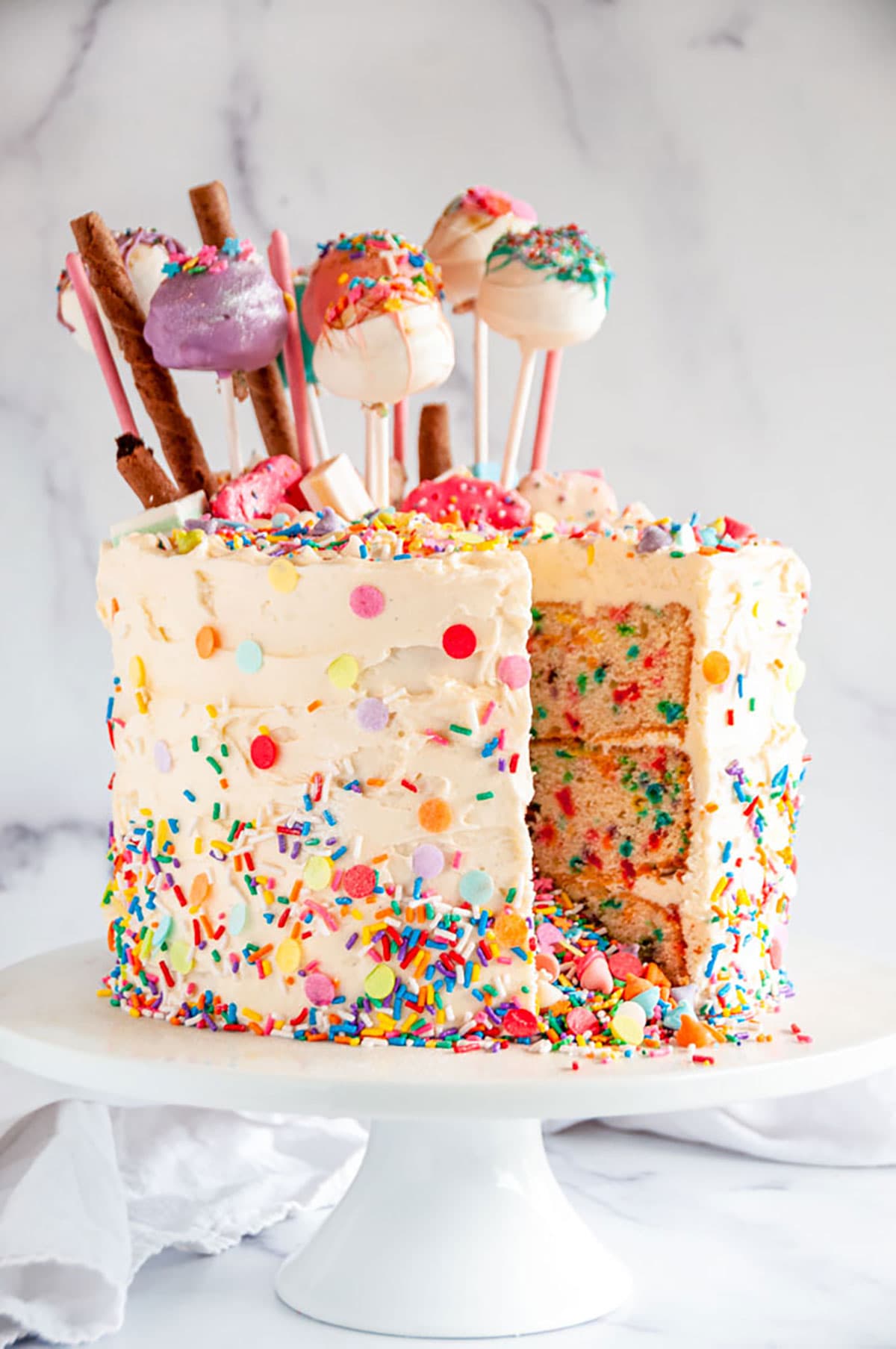 Birthday Surprise Confetti Cake with cake pops slice removed on white cake stand