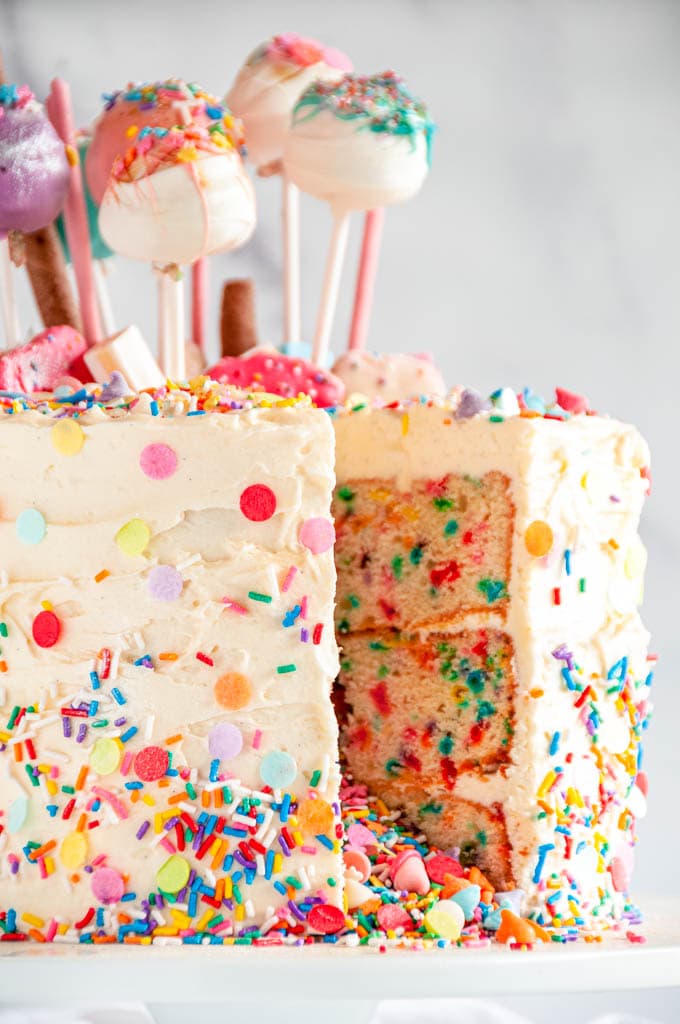 Birthday Surprise Confetti Cake with cake pops slice removed on white cake stand 