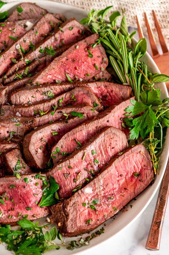 Easy Tender London Broil sliced on gray plate with fresh herbs