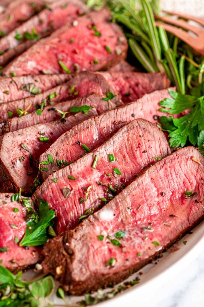 Easy Tender London Broil sliced on gray plate with fresh herbs
