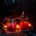 Halloween Black Cranberry Margarita in stemless glass with sanded sugar rims on black cloth and candle background