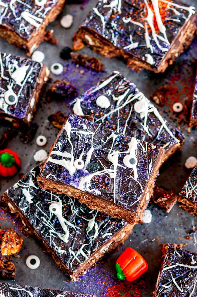 No Bake Chocolate Peanut Butter Pretzel Bars with Halloween sprinkles and candy pumpkins on parchment paper