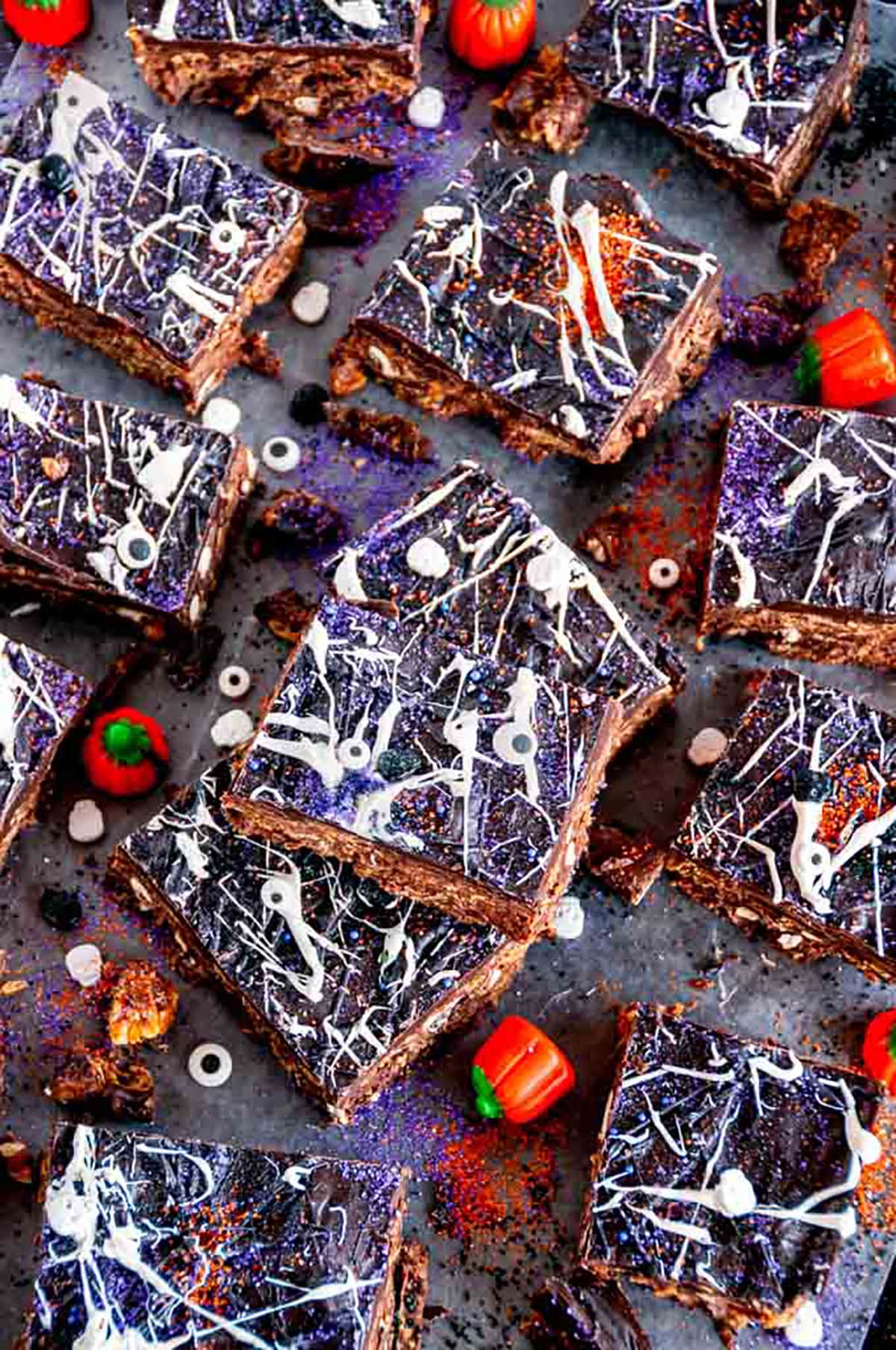 No Bake Chocolate Peanut Butter Pretzel Bars with Halloween sprinkles and candy pumpkins on parchment paper