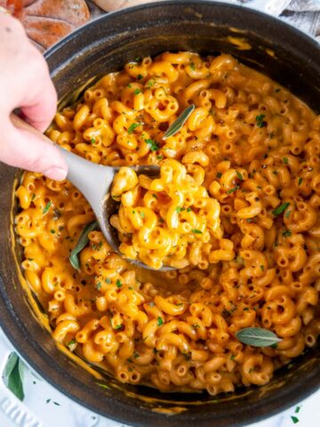 One Pot Pumpkin Mac and Cheese in white staub dutch oven with gray and wood spoon held in hand
