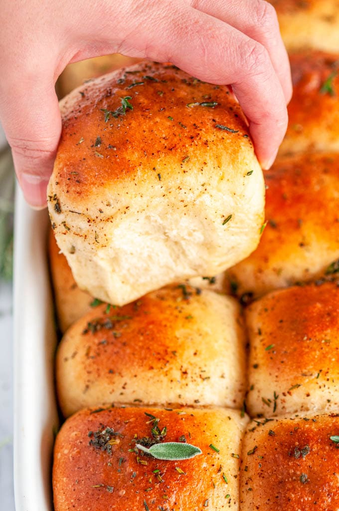 Brown Butter Herb Dinner Rolls held in hand and in white Staub baking dish