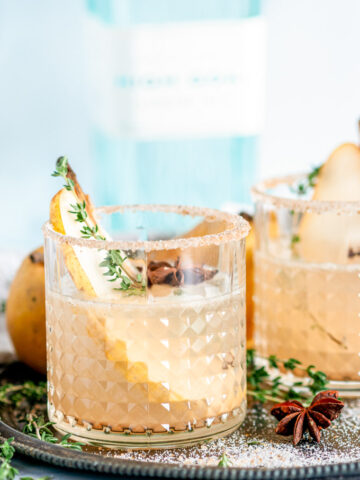 Spiced Pear Gin Fizz in cocktail glasses with sanded sugar rims on gray plate