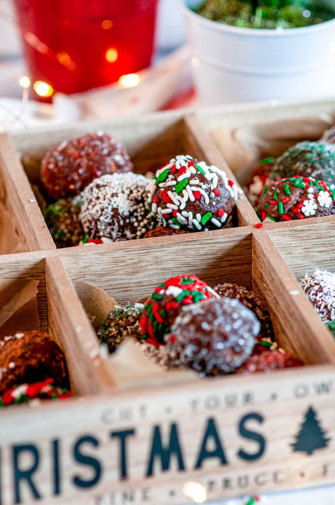 No Bake Chocolate Rum Balls in wooden cookie box with lights and potted plants