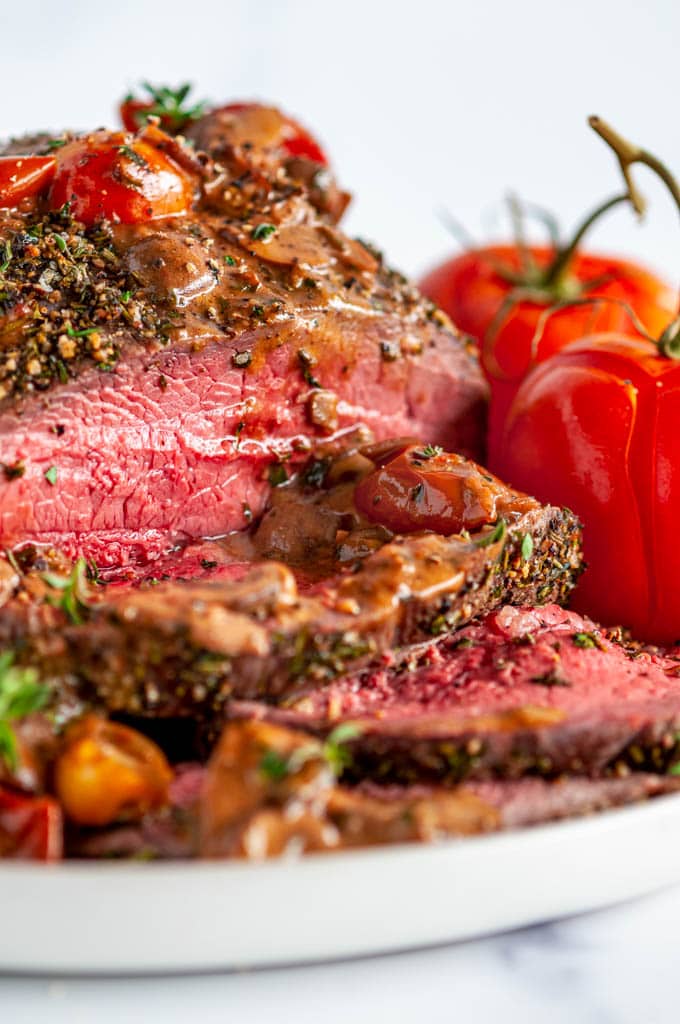 Pepper Crusted Top Sirloin Beef Roast with mushroom tomato skillet sauce sliced on white plate