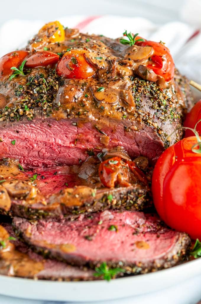 Pepper Crusted Top Sirloin Beef Roast with mushroom tomato skillet sauce sliced on white plate