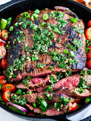 Skillet Flank Steak and Veggies with Chimichurri Sauce in lodge cast iron skillet with tomatoes and onion