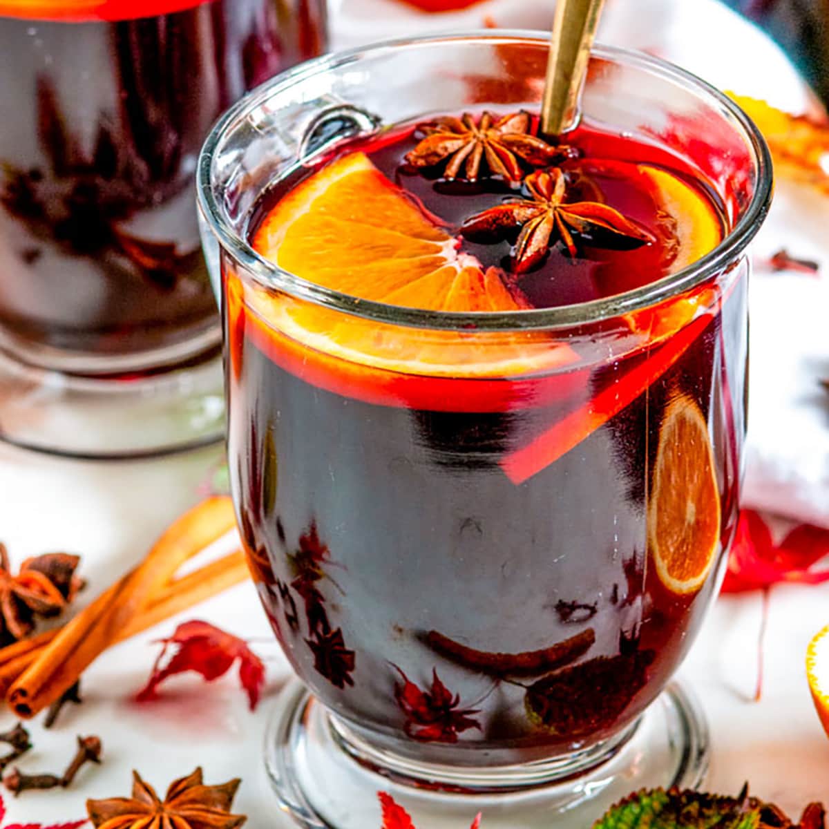 Spiced Holiday Mulled Wine in glass mugs with autumn leaves on white marble