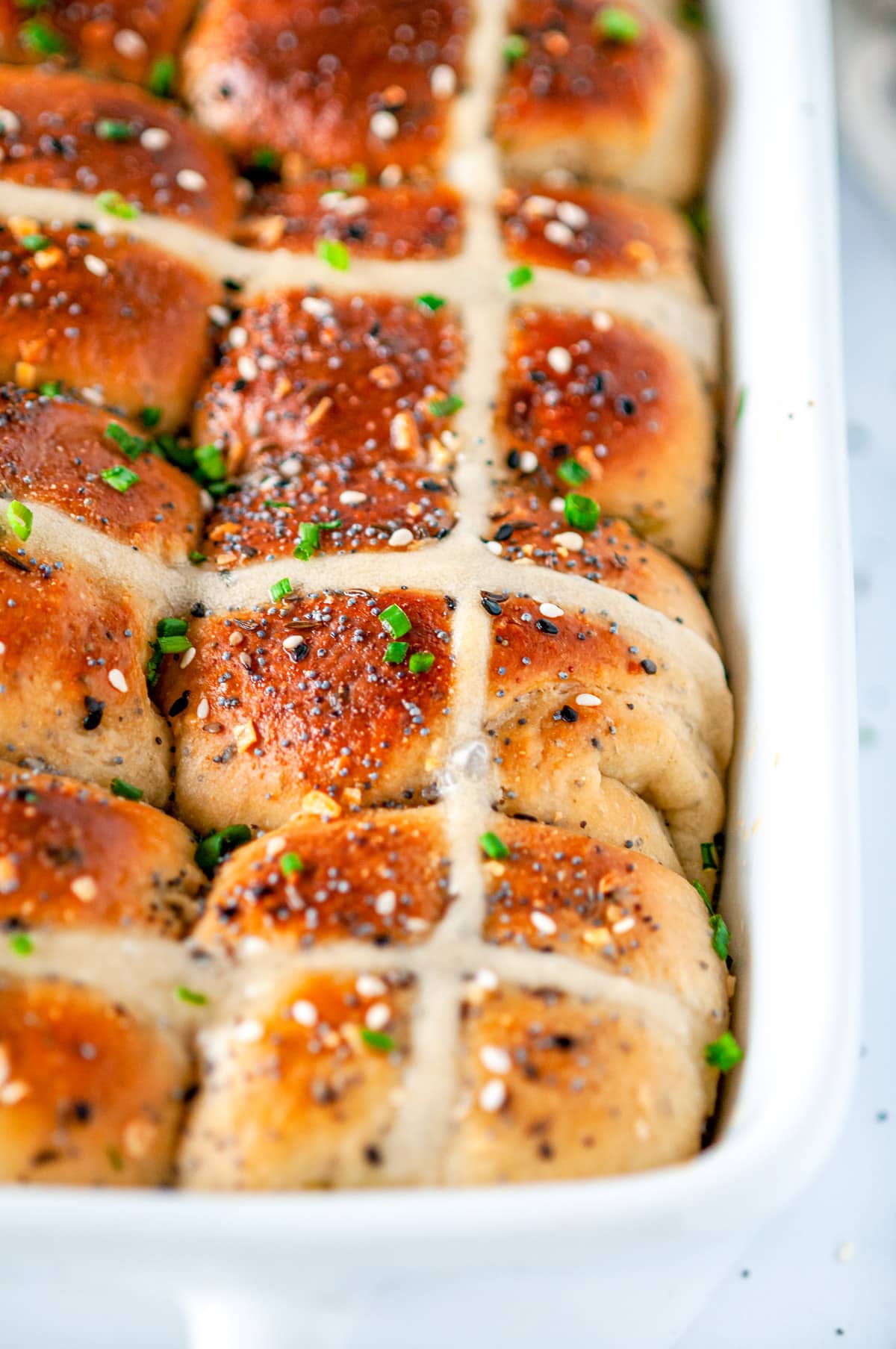 Everything Bagel Hot Cross Buns in white baking dish with sliced chives on white marble close up