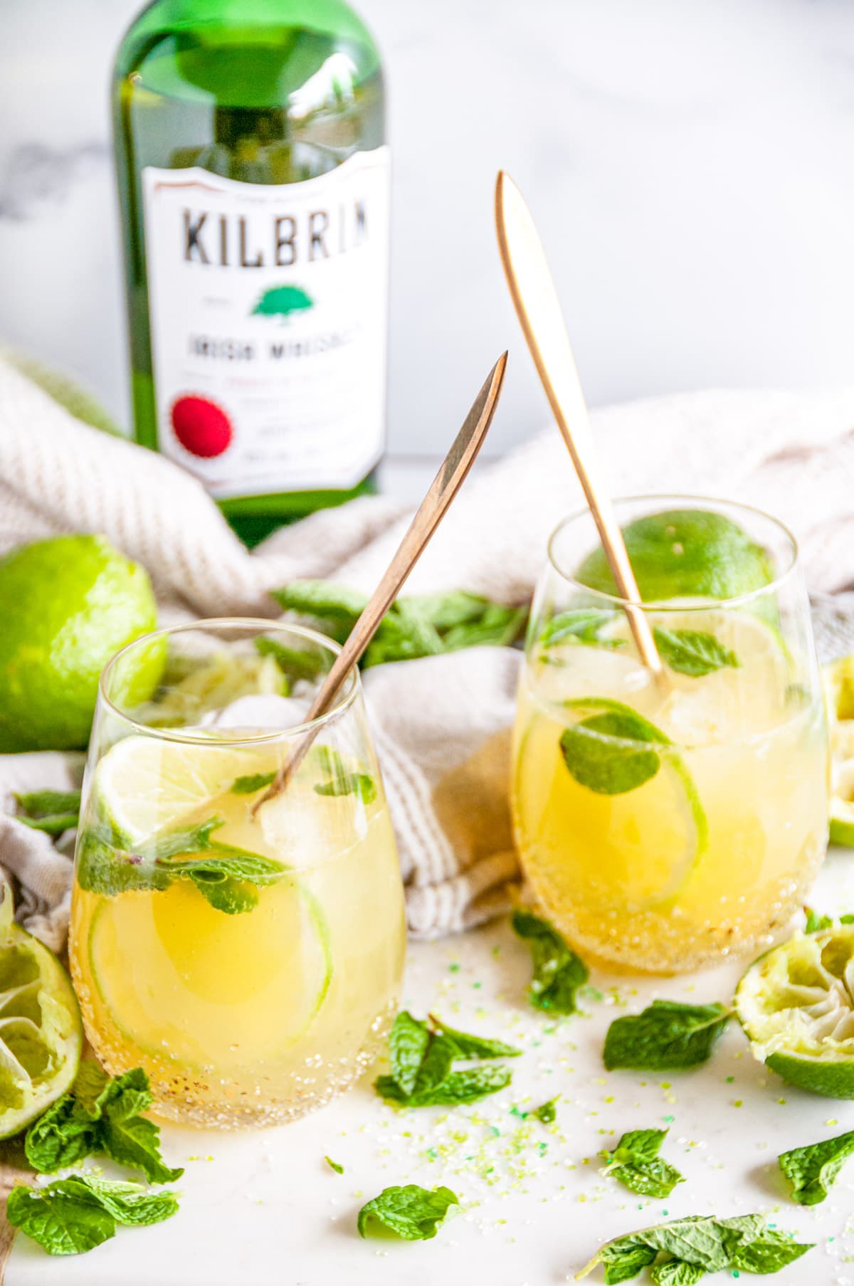 Irish Whiskey Mule Cocktail in stemless glasses with fresh lime and mint leaves on white marble