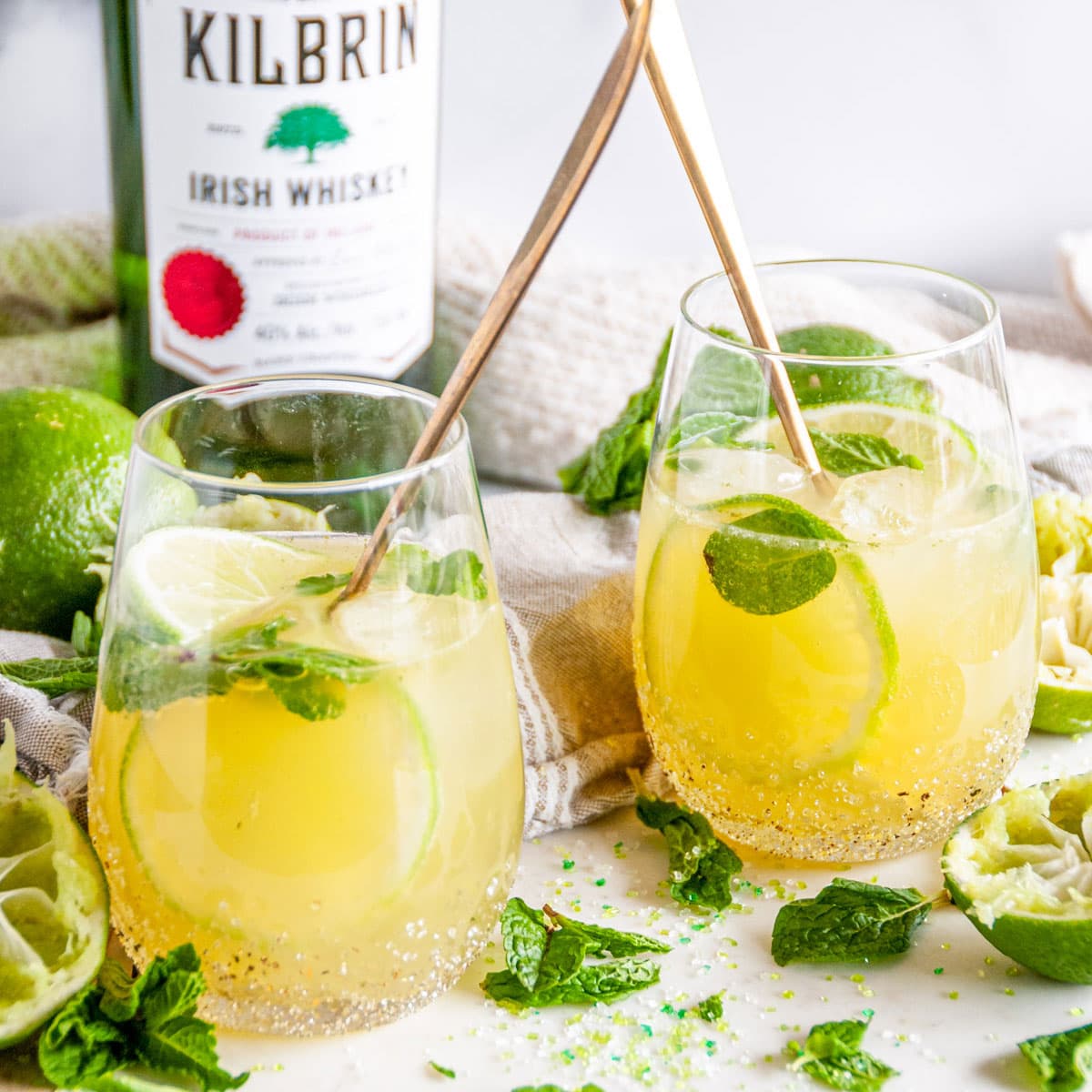 Irish Whiskey Mule Cocktail in stemless glasses with fresh lime and mint leaves on white marble