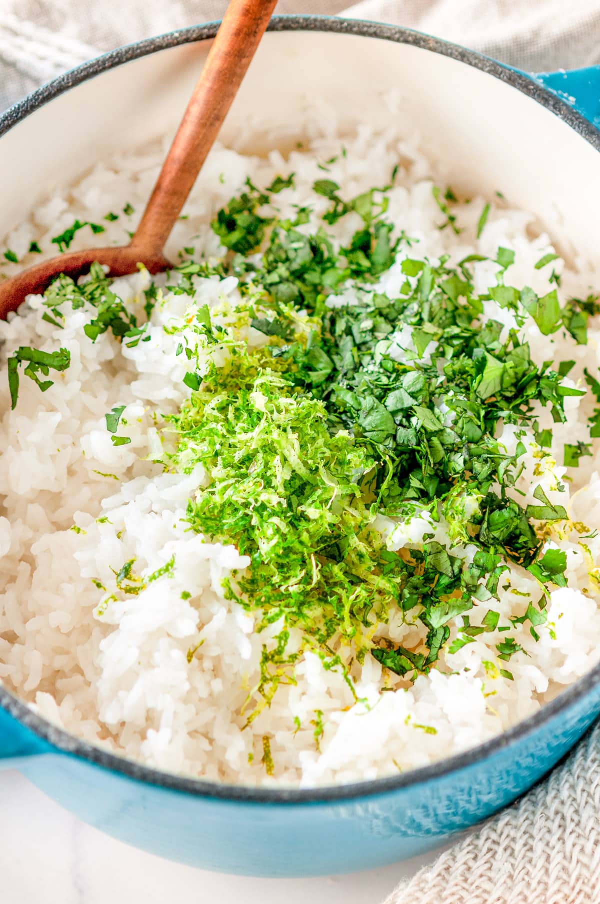 Cilantro lime rice in medium blue stock pot with wooden serving spoon before mixing together on white marble close up