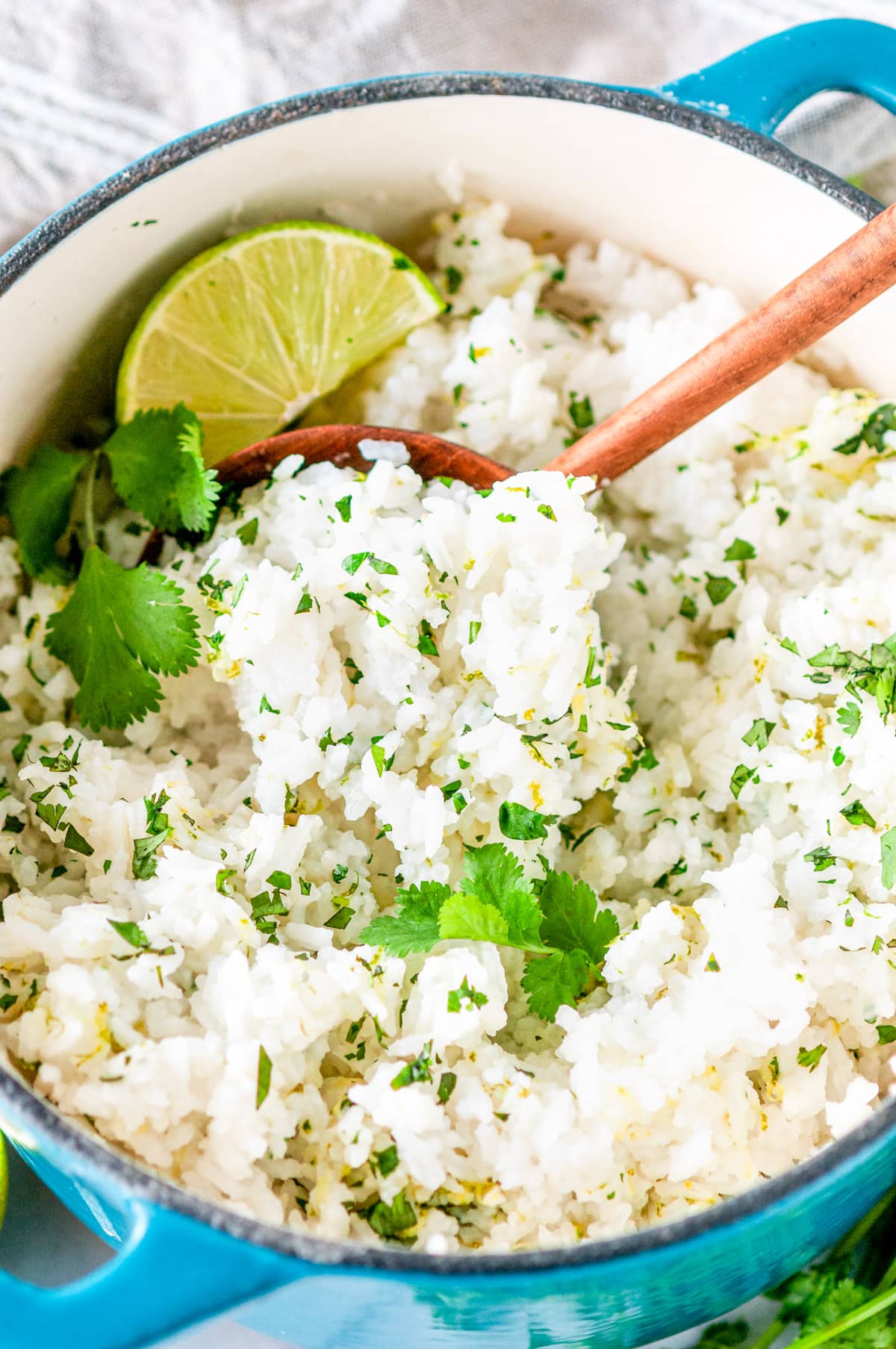 Cilantro lime rice in medium blue stock pot with wooden serving spoon on white marble