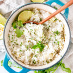 Cilantro lime rice in medium blue stock pot with wooden serving spoon on white marble overhead view