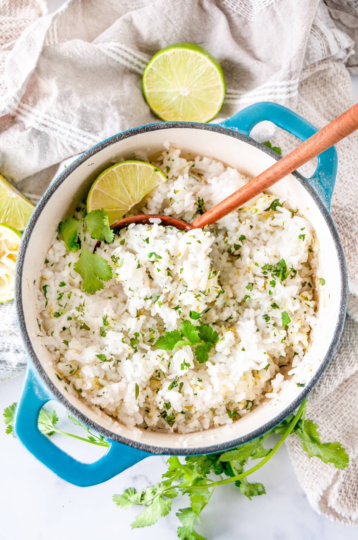 Cilantro lime rice in medium blue stock pot with wooden serving spoon on white marble overhead view
