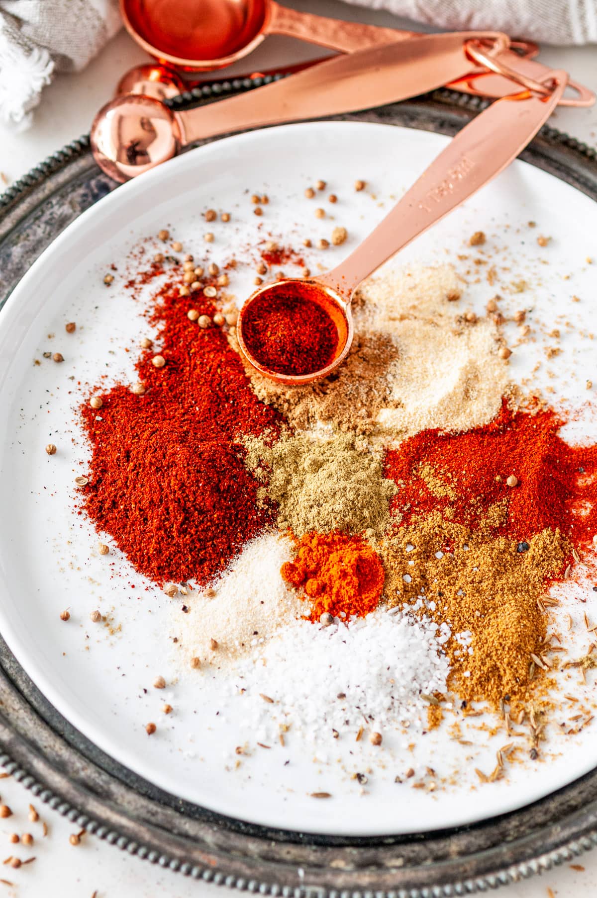 Mexican Spice Mix separated by ingredient on white plate with rose gold measuring spoons