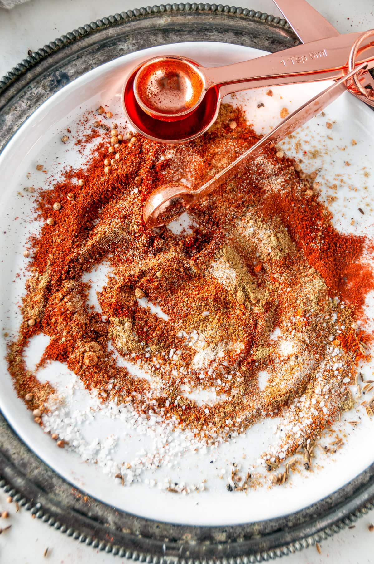 Mexican Spice Mix blended on white plate with rose gold measuring spoons overhead view