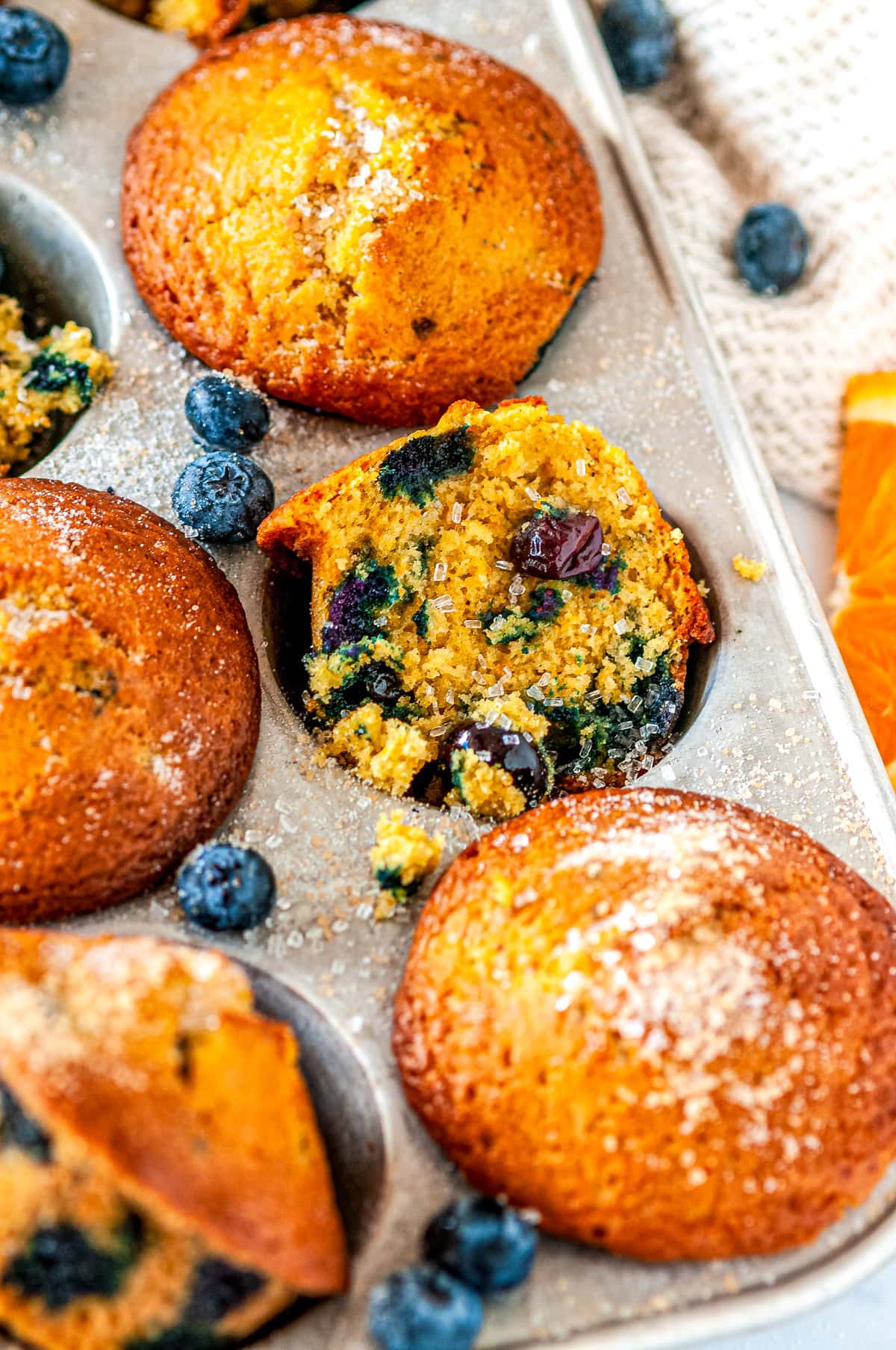 Zesty Orange Blueberry Muffins in silver muffin tray with sliced oranges and fresh blueberries on white marble side view close up