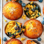Zesty Orange Blueberry Muffins in silver muffin tray with sliced oranges and fresh blueberries on white marble overhead view close up
