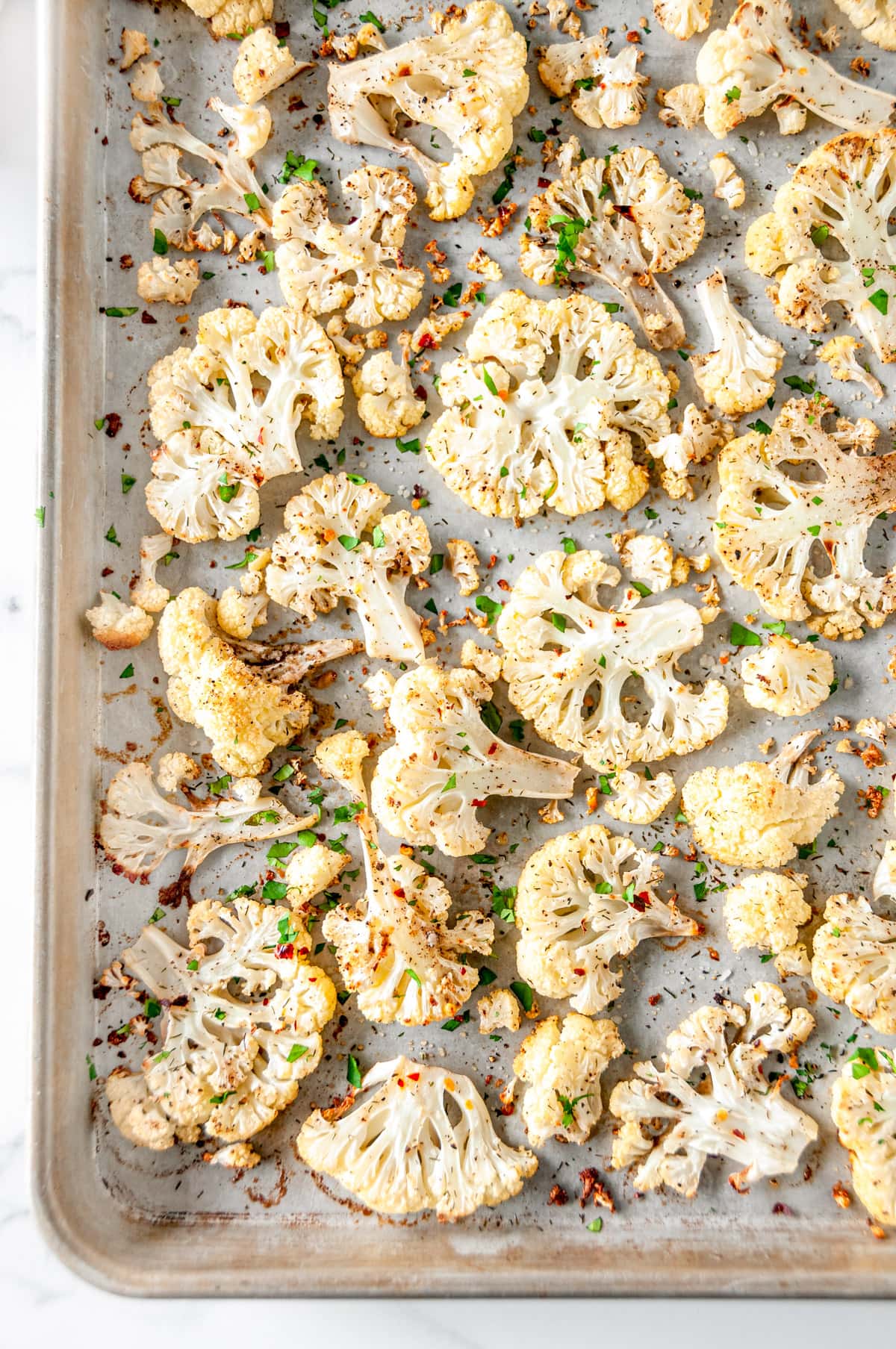 4-Ingredient Roasted Cauliflower on sheet pan with roughly chopped fresh parsley and red chili flakes