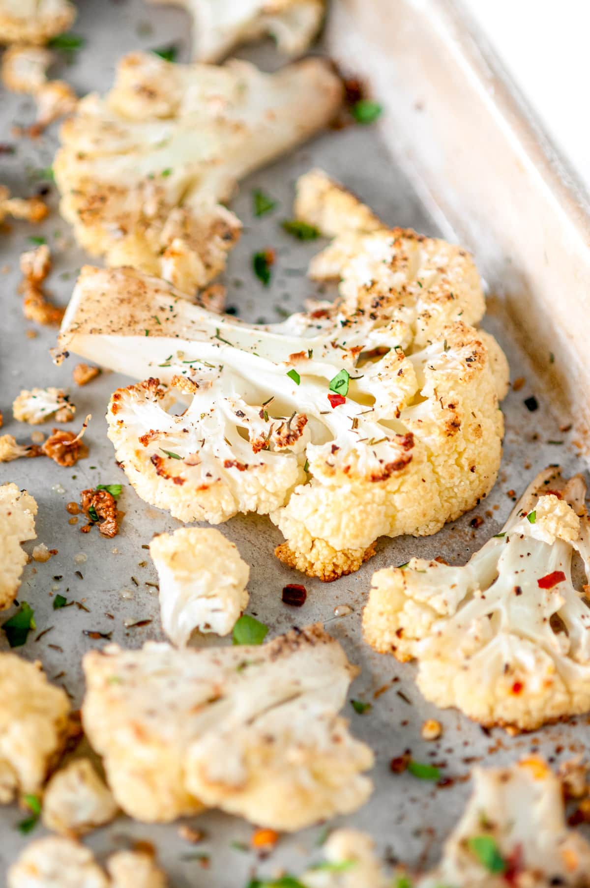 4-Ingredient Roasted Cauliflower on sheet pan with roughly chopped fresh parsley and red chili flakes close up