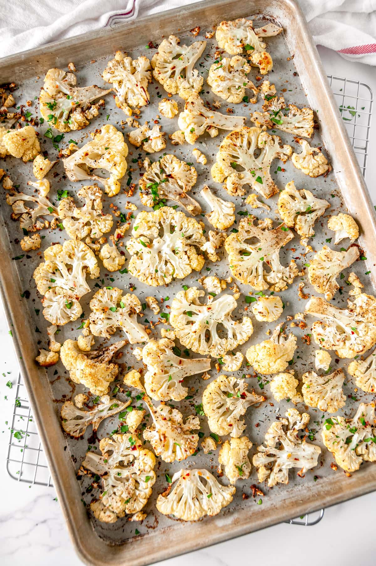 4-Ingredient Roasted Cauliflower on sheet pan with roughly chopped fresh parsley and red chili flakes