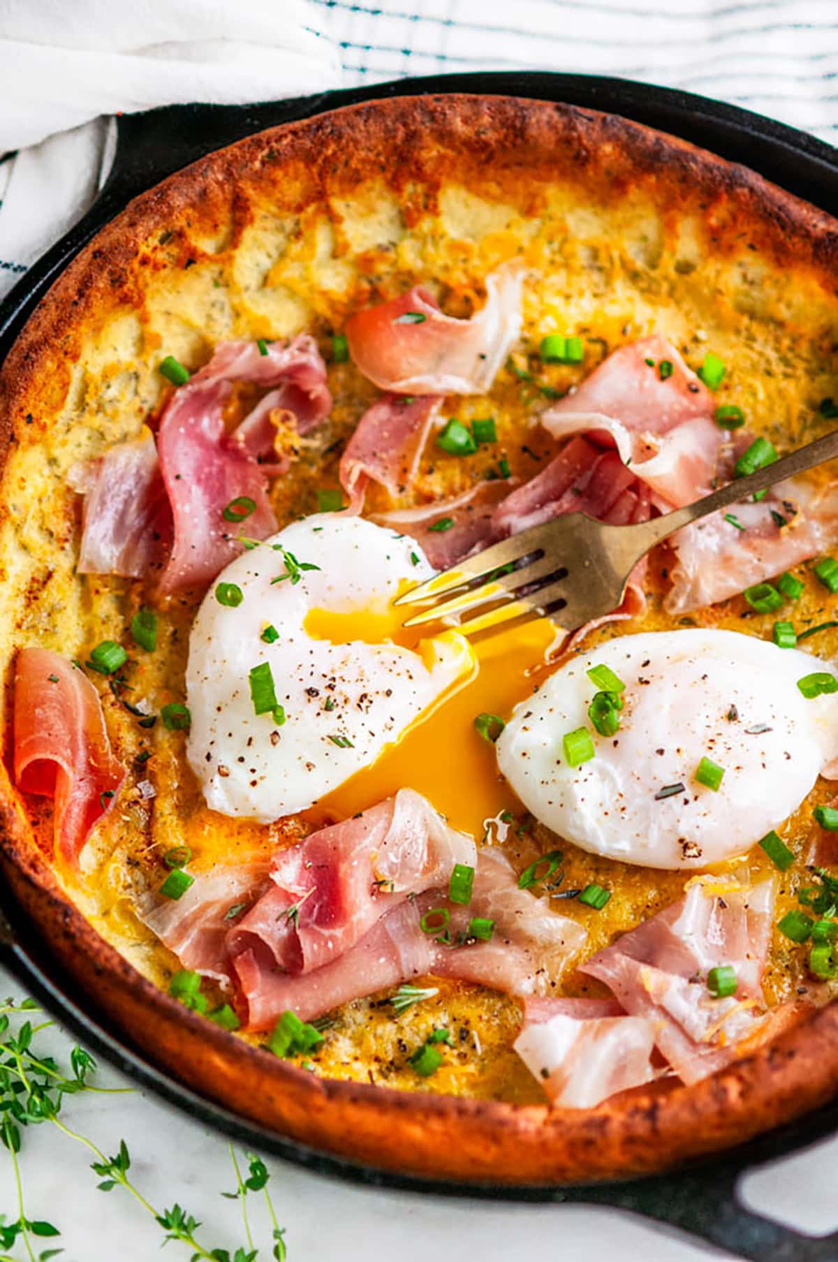 Perfect poached egg over head view on a savory dutch baby pancake in a cast iron skillet
