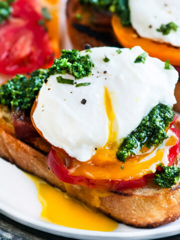 perfect poached egg drizzled with kale pesto on breakfast toast with a slice of tomato